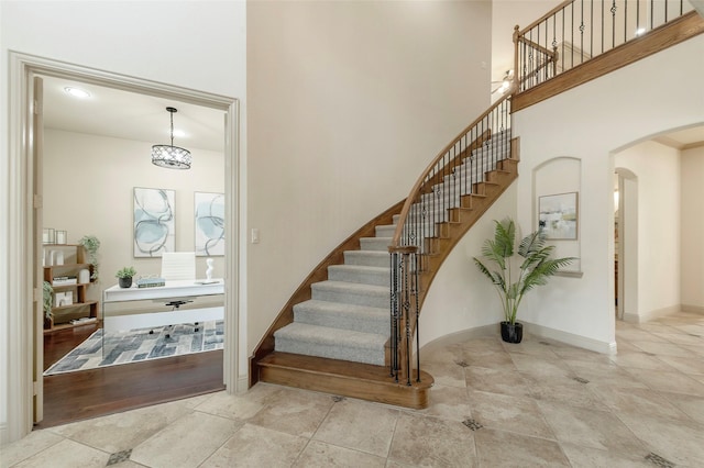 tiled entrance foyer with stairway, baseboards, a high ceiling, and arched walkways