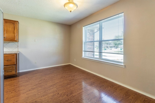 empty room with dark wood-style floors, a textured ceiling, and baseboards