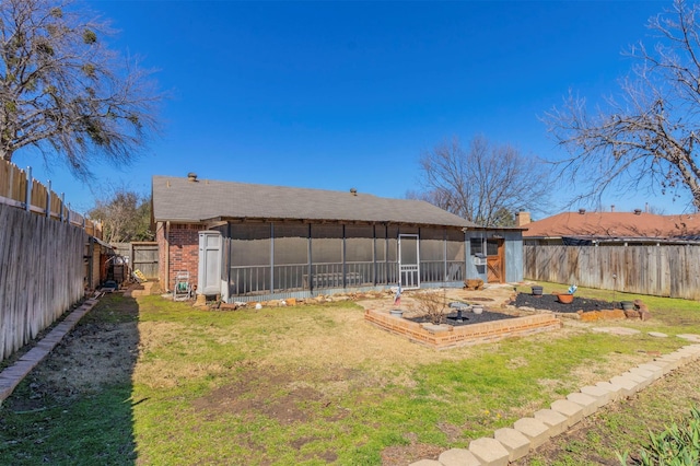 rear view of house with brick siding, a lawn, a fenced backyard, and a sunroom