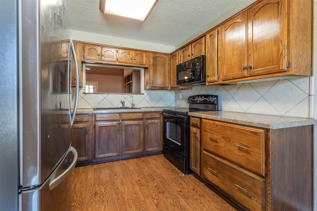 kitchen featuring light wood-type flooring, black appliances, brown cabinetry, and a sink