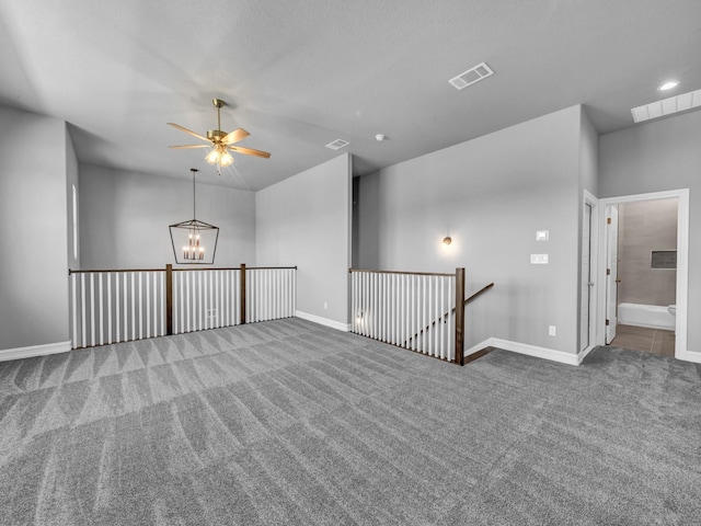 carpeted empty room featuring ceiling fan with notable chandelier, visible vents, and baseboards