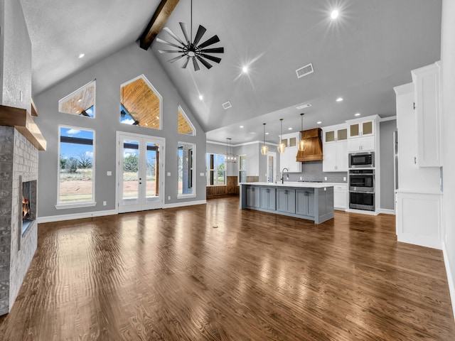 unfurnished living room with visible vents, beamed ceiling, a lit fireplace, a sink, and ceiling fan with notable chandelier