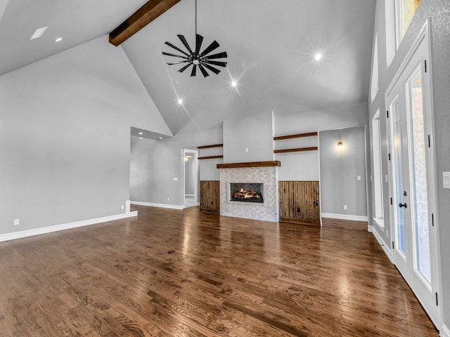 unfurnished living room featuring dark wood-style flooring, a tiled fireplace, high vaulted ceiling, beamed ceiling, and baseboards