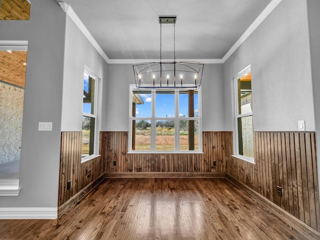 unfurnished dining area featuring a wainscoted wall, wooden walls, and a chandelier