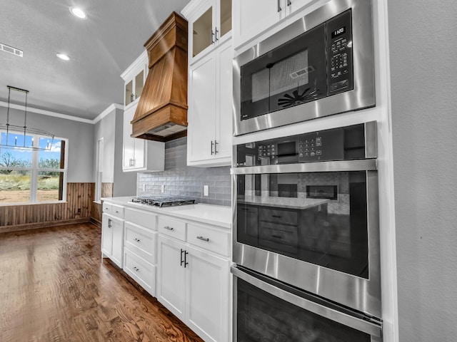 kitchen with dark wood finished floors, stainless steel appliances, visible vents, wainscoting, and premium range hood