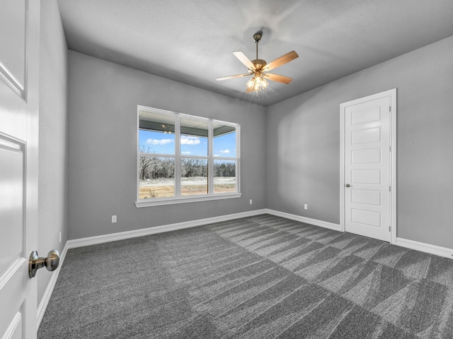 empty room featuring baseboards, dark colored carpet, and a ceiling fan