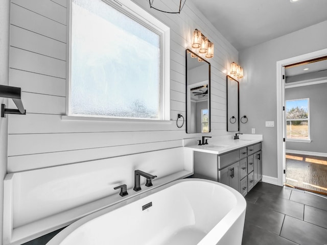 bathroom with double vanity, a freestanding bath, baseboards, and a sink