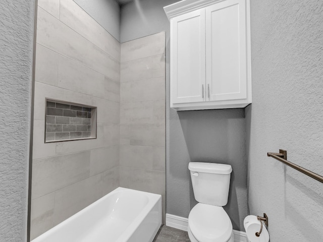 bathroom featuring toilet, washtub / shower combination, baseboards, and a textured wall