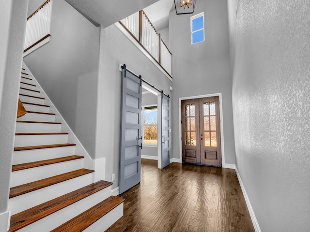 entrance foyer with a barn door, wood finished floors, baseboards, french doors, and stairway