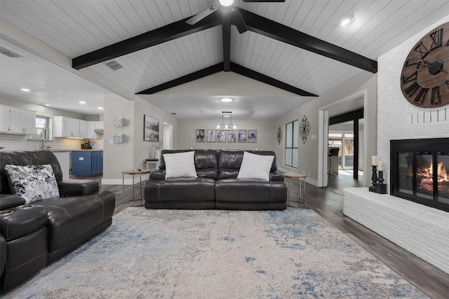 living room with dark wood-style flooring, visible vents, lofted ceiling with beams, a brick fireplace, and baseboards