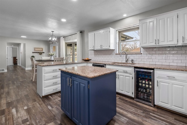 kitchen with a center island, white cabinetry, a sink, blue cabinets, and beverage cooler