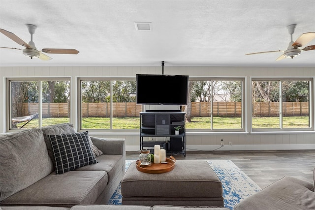 living area with a ceiling fan, visible vents, a textured ceiling, and wood finished floors