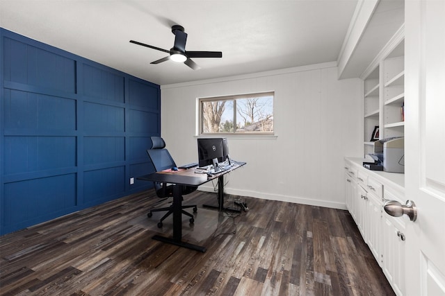 unfurnished office featuring dark wood-style floors, ceiling fan, baseboards, and a decorative wall