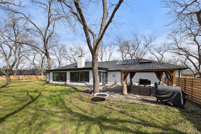 back of house with a lawn, solar panels, a patio, a fenced backyard, and a chimney