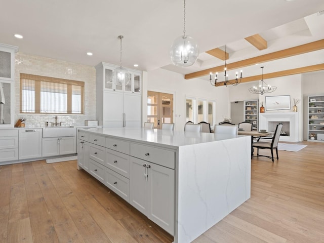 kitchen with light wood-style flooring, beam ceiling, a sink, and a center island