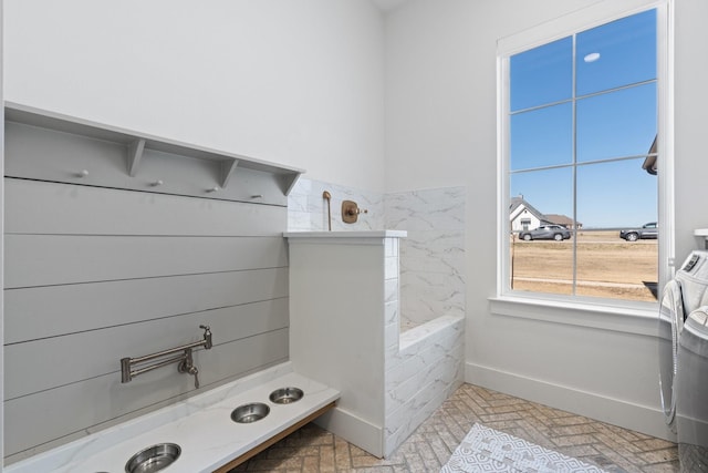 bathroom with brick floor, washer / clothes dryer, tiled shower, and baseboards