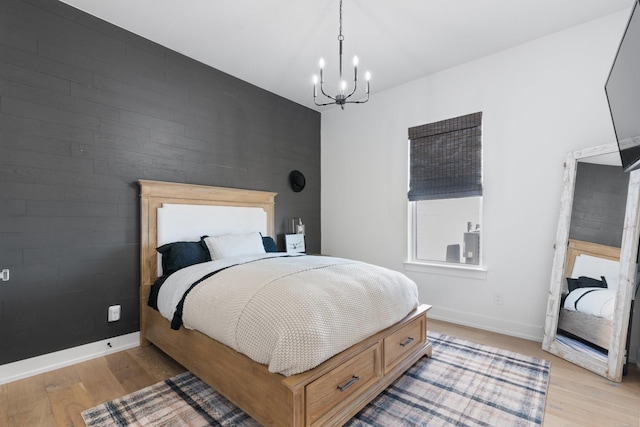 bedroom featuring light wood finished floors, an accent wall, baseboards, and an inviting chandelier