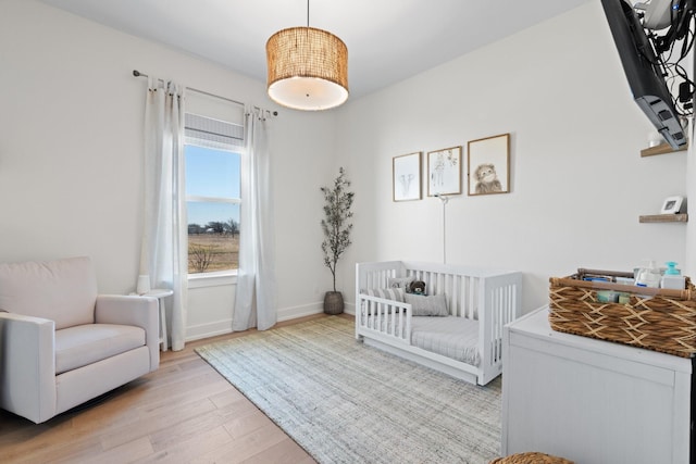 bedroom featuring light wood-style floors, a crib, and baseboards