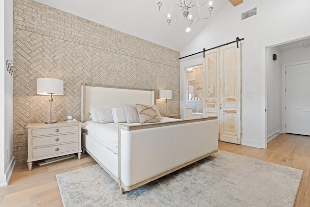 bedroom with lofted ceiling, a barn door, an accent wall, visible vents, and light wood finished floors