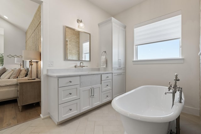 ensuite bathroom featuring vaulted ceiling, a soaking tub, connected bathroom, and vanity