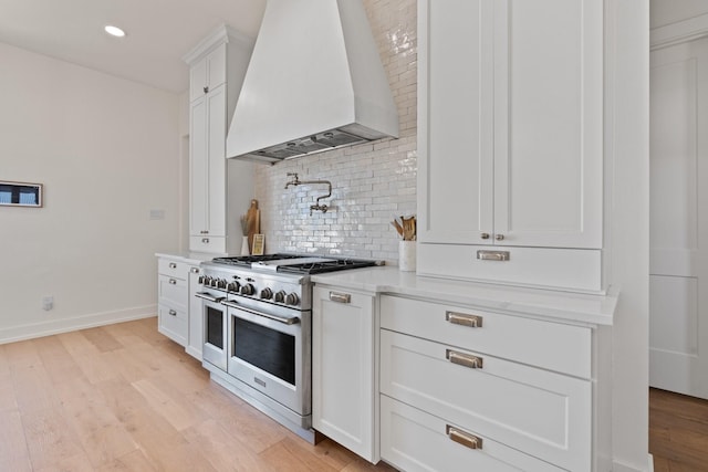 kitchen with light wood-style flooring, custom range hood, double oven range, white cabinetry, and backsplash