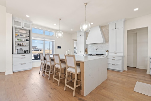 kitchen featuring light wood finished floors, a kitchen island with sink, custom exhaust hood, and backsplash