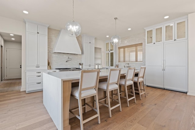 kitchen featuring light countertops, tasteful backsplash, light wood-type flooring, and custom exhaust hood