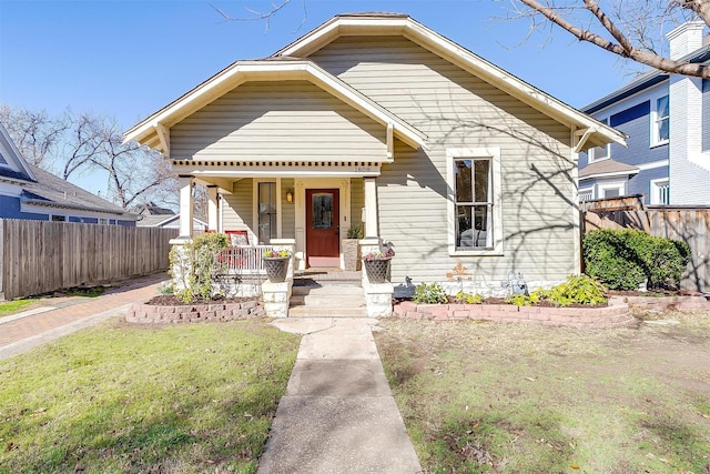 bungalow-style home with a porch, fence, and a front lawn