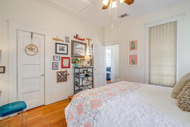 bedroom with wood finished floors, a ceiling fan, baseboards, visible vents, and attic access