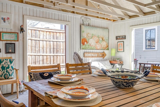 dining area featuring vaulted ceiling and wood walls