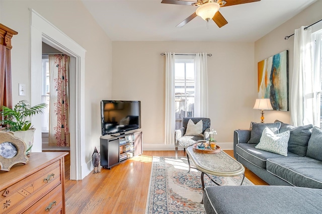 living area featuring ceiling fan, light wood-style flooring, and baseboards