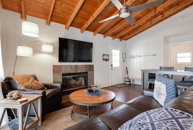 living area with beam ceiling, ceiling fan, wood finished floors, a tile fireplace, and wooden ceiling