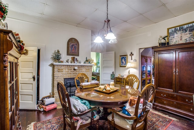 dining area featuring dark wood-type flooring, a fireplace, a paneled ceiling, and a notable chandelier