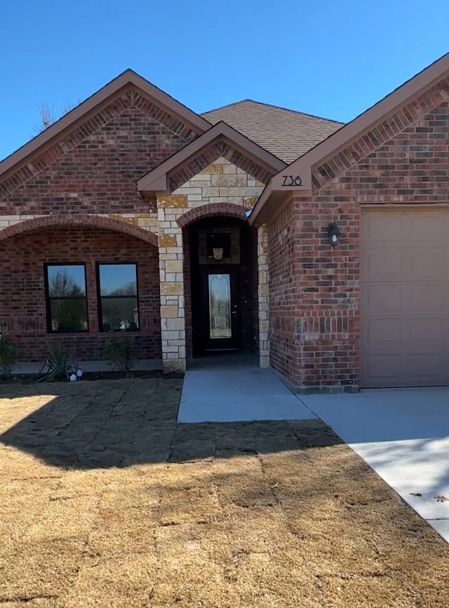 view of exterior entry featuring brick siding, roof with shingles, and an attached garage