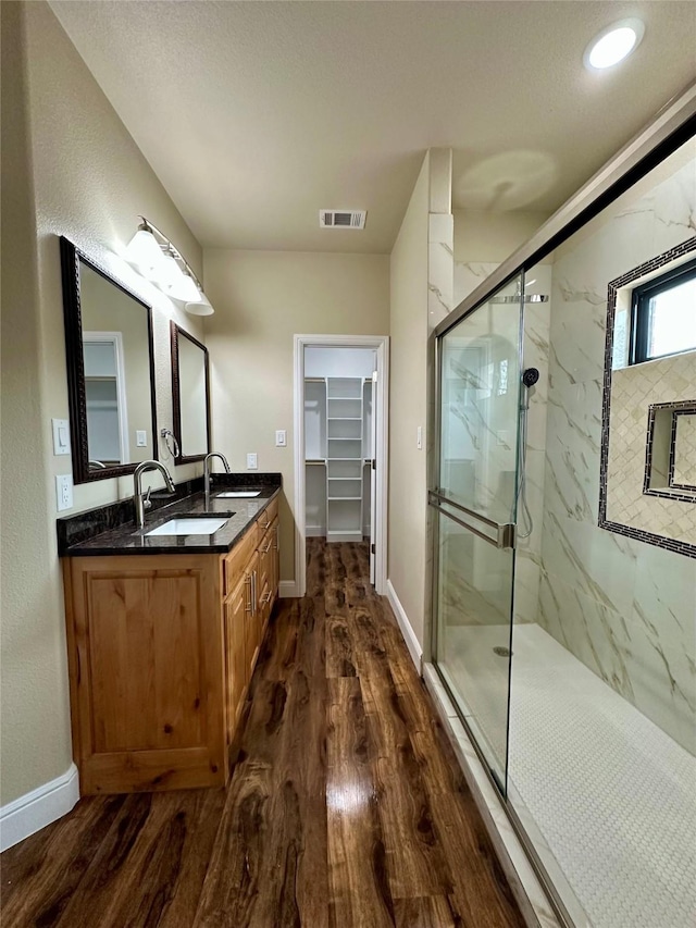 bathroom with visible vents, a sink, a marble finish shower, and wood finished floors