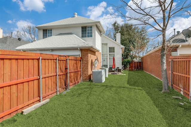 rear view of house featuring central AC unit, a fenced backyard, brick siding, a yard, and roof with shingles