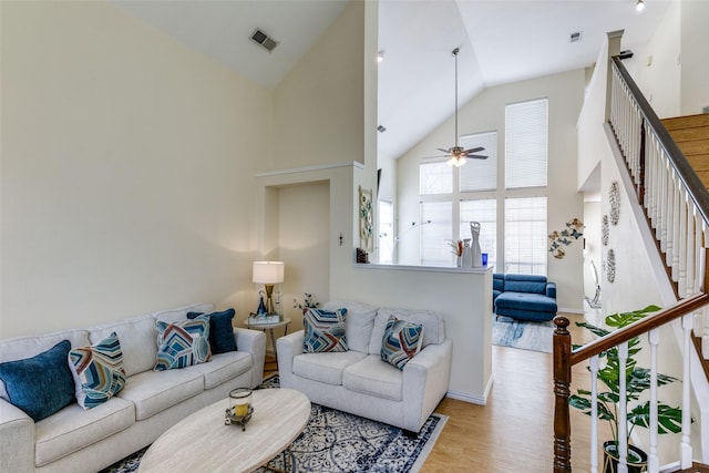 living room with high vaulted ceiling, visible vents, a ceiling fan, stairs, and light wood finished floors