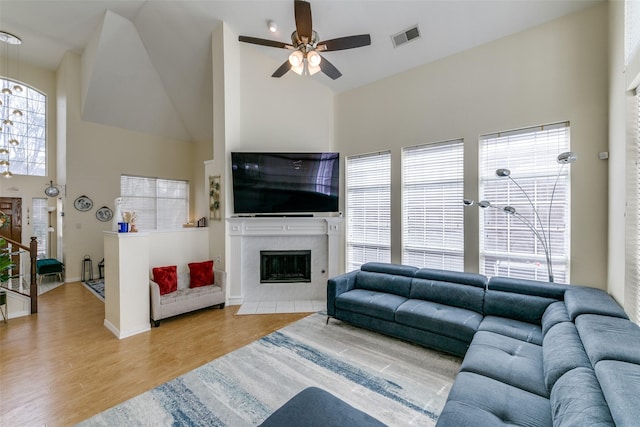 living area featuring a high ceiling, wood finished floors, visible vents, a ceiling fan, and a tiled fireplace