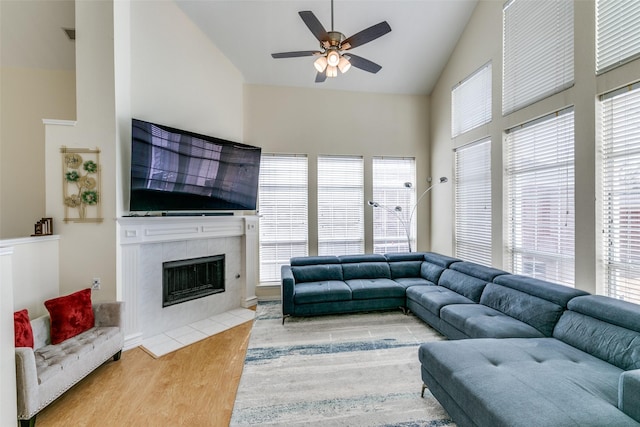 living room featuring ceiling fan, high vaulted ceiling, wood finished floors, and a tile fireplace