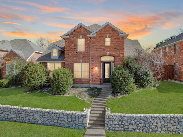 traditional home featuring a yard, brick siding, and roof with shingles