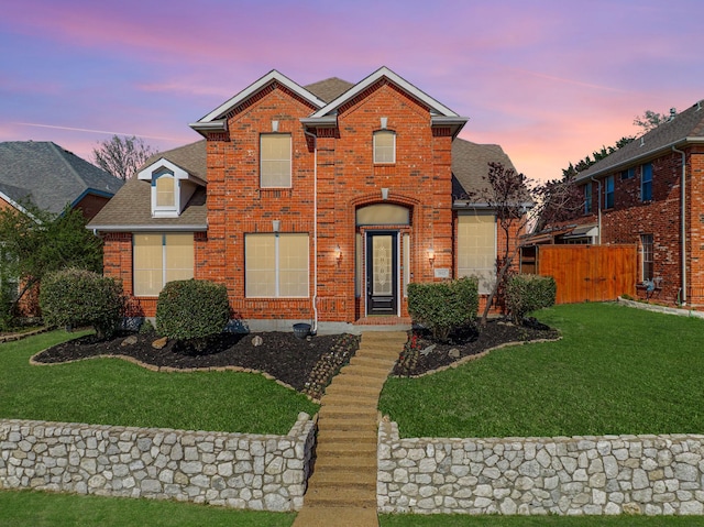 traditional-style house featuring brick siding, roof with shingles, a front lawn, and fence