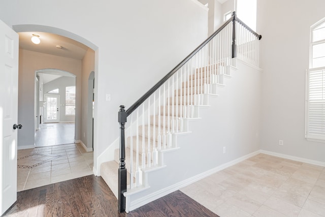 staircase with arched walkways, a high ceiling, baseboards, and wood finished floors