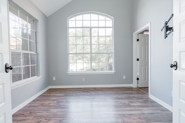 empty room featuring lofted ceiling, wood finished floors, and baseboards