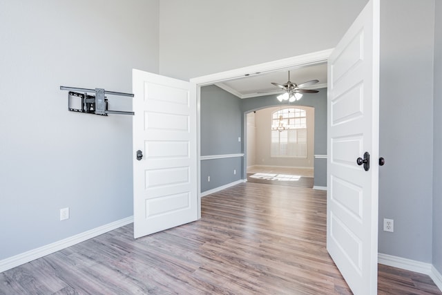 empty room with baseboards, arched walkways, a ceiling fan, wood finished floors, and crown molding