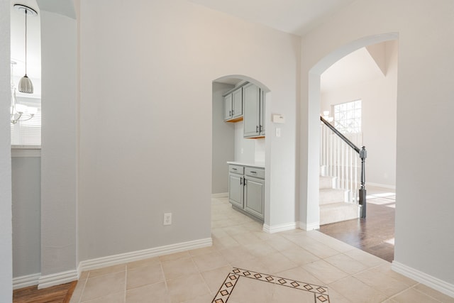 corridor featuring stairs, arched walkways, baseboards, and light tile patterned floors