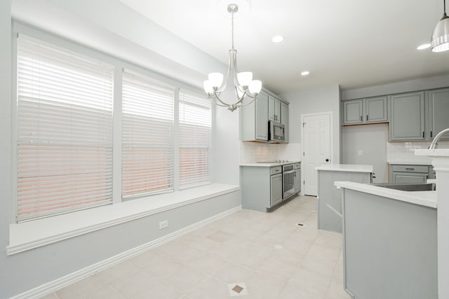 kitchen with stainless steel microwave, gray cabinets, decorative backsplash, and an inviting chandelier