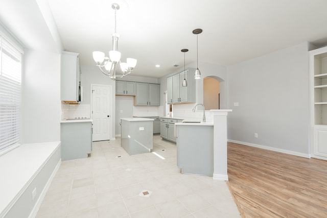 kitchen with a sink, gray cabinets, arched walkways, an inviting chandelier, and a peninsula
