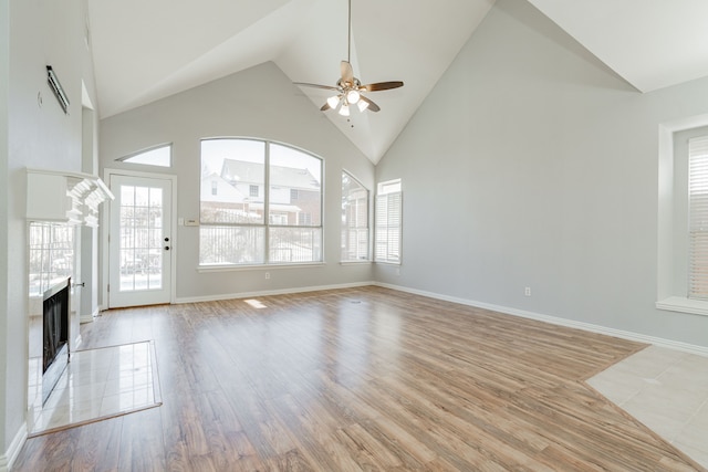 unfurnished living room with light wood finished floors, baseboards, a tiled fireplace, high vaulted ceiling, and ceiling fan