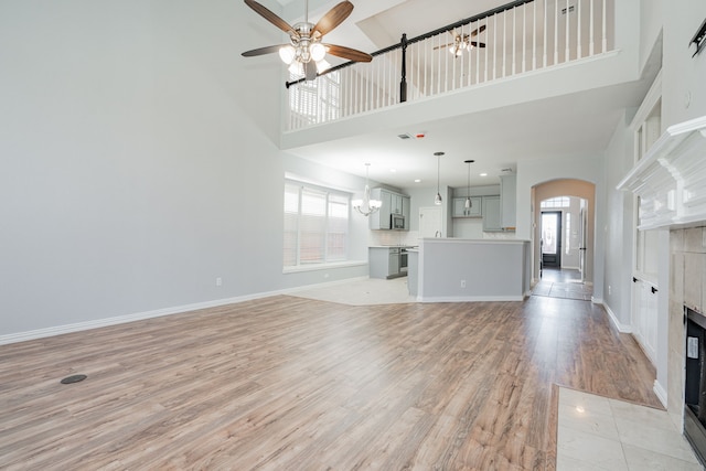 unfurnished living room featuring light wood-style floors, a fireplace, arched walkways, and ceiling fan with notable chandelier