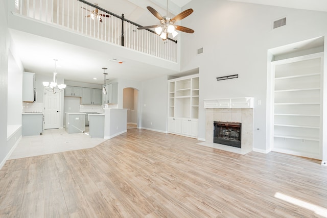 unfurnished living room with arched walkways, a tile fireplace, ceiling fan with notable chandelier, visible vents, and light wood-style floors